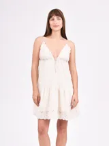 Vestido corto color crudo con breteles finos, escote en V con detalle de puntilla y falda con volado y bordado calado.