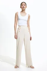 Pantalón de vestir color crema, de tiro alto y corte palazzo, con detalle de doble botonadura dorada en la parte superior.