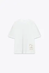 Camiseta blanca de algodón, corte recto, cuello redondo y manga corta. Tiene una etiqueta estampada en el frente.
