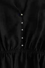 Vestido corto negro con escote en V profundo, botones forrados adelante y cinturón para atar extraíble. Modelo de corte holgado con canesú de doble capa, hombros fruncidos, mangas globo largas y puños anchos con botones forrados. Elástico revestido en la cintura y pollera con leve vuelo.