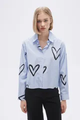 Camisa celeste a rayas verticales blancas, con cuello clásico, cierre frontal con botones y estampado de corazones negros.
