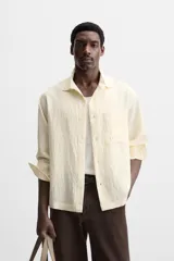 Camisa color crema de corte relaxed fit, confeccionada en tejido con mezcla de viscosa. Tiene cuello solapa, manga larga con puños abotonados, bolsillo de parche en el pecho y cierre frontal con botones.