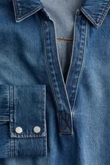 Camisa de denim azul con cuello abierto y canesú con pliegue de caja en la espalda. Modelo de corte holgado con hombros caídos y mangas largas con botones a presión en los puños. Bajo recto, algo más largo atrás, con aberturas laterales.