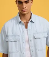 Camisa masculina de jeans celeste con estampa de rayas verticales, corte boxy, cuello inglés, manga corta, cierre abotonado y bolsillos frontales.