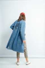 Tapado largo de jeans azul con bordado en la espalda, cuello camisero, bolsillos laterales y cierre frontal con botones.