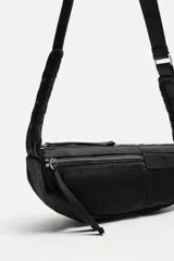 Bandolera negra de tela técnica con correa ajustable. Tiene un compartimento principal con cierre de cremallera, un bolsillo interior plano con cremallera y dos bolsillos frontales, uno de ellos con cremallera.