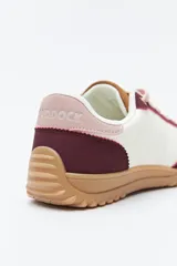 Zapatilla urbana de mujer con silueta retro, combinando paneles de gamuza marrón oscuro y material color crema en el cuerpo. Presenta detalles en color bordó en el talón y cordones beige. La suela es robusta de color marrón claro con relieve.