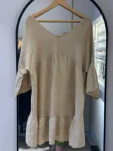 Vestido corto color beige de lino, con escote en V, mangas acampanadas y un volante fruncido en el ruedo.