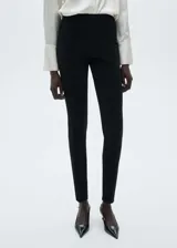 Pantalón negro de tejido de punto ligero con cintura elástica, corte slim fit, diseño largo, detalle de costuras y cierre con cremallera en los bajos.