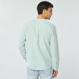 Camisa celeste claro de lino con cuello mao, manga larga con puños abotonados y bolsillo de parche en el pecho.