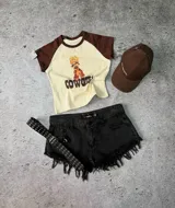 Remera corta color crema con mangas marrones, estampado de una cowgirl y la palabra "COWGIRL" en el frente.