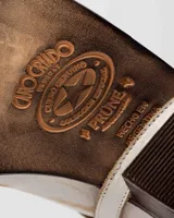 Bota texana de cuero negro con detalles desgastados y bordados en color blanco. Tiene una correa desmontable con hebilla metálica y un taco de madera.