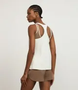 Musculosa deportiva de mujer, color blanco y marrón, con diseño de recortes diagonales y ribetes en contraste. Presenta un pequeño logo bordado en el pecho.