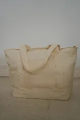 Bolso tote de lona color crudo con asas de hombro. Decorado con parches bordados de motivos playeros y pañuelo rojo estampado atado a una de las asas.