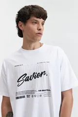Remera blanca de manga corta con estampado frontal que incluye la palabra 'Savior' en letras cursivas negras y otros textos en tipografía sans-serif. Corte regular.