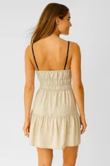 Vestido corto color beige, con breteles finos negros, escote recto y lazo decorativo en el centro del pecho. Tiene corte imperio con falda de dos niveles.