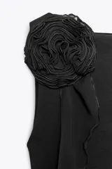 Top negro de cuello redondo y sin mangas, con detalle de flor con volumen en el hombro.