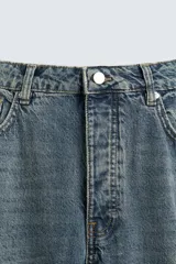 Pantalón de denim color beige, corte relaxed fit, con bolsillos laterales tipo cargo con solapa y cierre de botón. Cierre frontal con botón y cremallera.
