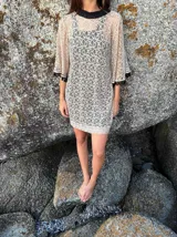 Vestido corto de encaje beige con mangas al sesgo y guarda de caireles negros en el reborde. Incluye vestido básico negro para usar debajo.