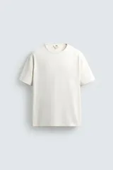 Camiseta color crudo de corte relaxed fit, confeccionada en tejido compacto de algodón. Tiene cuello redondo con ribete doble y mangas cortas.