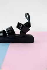 Sandalias negras charoladas con plataforma, tiras anchas y hebilla al tobillo.