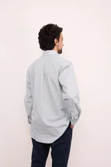 Camisa celeste con rayas verticales blancas, de corte clásico, con cuello abotonado, manga larga y bolsillo en el pecho.
