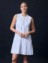 Vestido corto blanco de algodón y rayón, sin mangas, con cuello a la base, abertura central con botones y detalle plisado en la delantera. Incluye bolsillos laterales.