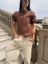 Camisa color ladrillo confeccionada en lino, con cuello mao, mangas cortas abullonadas y cierre frontal con botones.