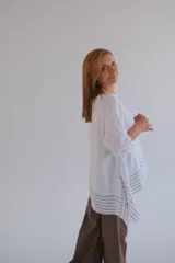 Blusa blanca de lino con corte asimétrico y rayas horizontales en el ruedo.