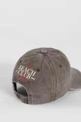 Gorra de gabardina color verde oliva con bordado frontal "Beach Club" en color rojo y detalle de etiqueta roja en el lateral.