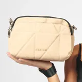 Bandolera color beige con diseño acolchado en forma de rombos. Tiene correa larga regulable de color negro, cierre superior y logo de la marca en el frente.