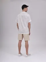 Camisa de manga corta con estampado de hojas color verde sobre fondo beige, cuello solapa y bolsillo en el pecho.