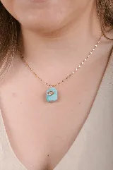 Collar con dije de piedra natural de jade color verde agua, con detalle de ojo turco en acero dorado. La cadena es de eslabones chatos en acero dorado.