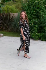 Camisola larga de muselina negra con estampado de lunares blancos, cuello camisero y manga corta. Presenta un corte holgado y abotonadura frontal completa.