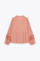 Blusa color rosa pálido de algodón con cuello redondo con volantes y cordón. Escote pico y manga larga. Detalle de bordados combinados a contraste color marrón. Cierre frontal con botones.