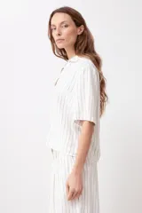 Blusa de lino a rayas verticales blancas y negras, con cuello camisero y mangas cortas.