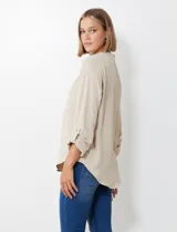Blusa de gasa color beige, con cuello a la base y escote en V. Manga larga con presilla y botón para ajustar el largo.