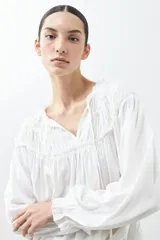 Blusa blanca de estilo boho con escote con volados y lazos, mangas largas abullonadas con puños elásticos.
