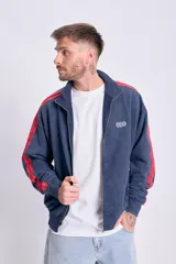 Campera deportiva con cierre frontal, cuello alto y puños y cintura acanalados. Color azul marino con efecto desgastado y dos franjas rojas a lo largo de las mangas. Presenta un pequeño logo bordado en el pecho.