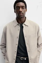 Camisa color crema de corte relaxed fit, confeccionada en tejido de mezcla de algodón suave al tacto. Tiene cuello solapa, manga larga con puños abotonados, un bolsillo de parche en el pecho y cierre frontal con botones.