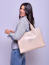 Cartera tipo tote bag de cuero color beige claro, con asas de hombro y un logo circular grabado en el centro.