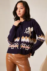 Cardigan azul marino de punto con cuello redondo y cierre frontal con botones. Presenta diseño con motivos geométricos en tonos beige, blanco y rosa, y un dibujo de un cupido en el pecho.