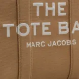 Bolso tipo tote de jacquard color negro con inscripción frontal 'THE TOTE BAG MARC JACOBS' en color blanco. Presenta un diseño de gran capacidad con cierre de cremallera superior, asas dobles para llevar al hombro o en la mano y bordes laterales en contraste con texto.