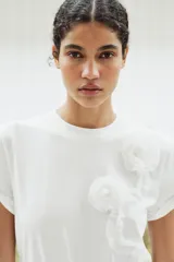 Camiseta blanca de algodón de manga corta y cuello redondo con detalle de flores en relieve en el frente.
