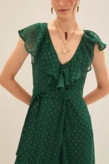 Vestido largo cruzado color verde esmeralda con estampado de puntos dorados. Presenta escote en V con volados en los hombros y en el borde del cruce, y un lazo para ajustar a la cintura.