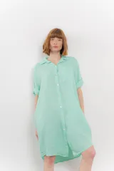 Vestido camisero corto color verde oliva, confeccionado en lino 100%. Tiene botones en la parte delantera, cuello camisero, mangas cortas con botón para arremangar y bolsillos laterales.