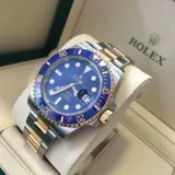 Reloj Rolex Submariner réplica Triple AAA, con caja y brazalete de acero inoxidable, bisel azul y detalles dorados.
