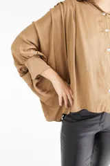 Camisa color beige de satén con corte holgado, cuello camisero y mangas largas con puños abotonados.