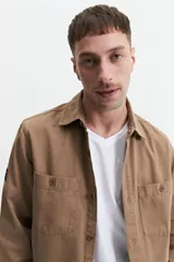 Sobrecamisa color marrón claro de twill de algodón, con cuello clásico, cierre frontal con botones a tono, dos bolsillos de parche con solapa abotonada en el pecho y mangas largas con puños abotonados.