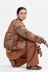 Campera puffer color camel con estampado de paisaje en azul marino, cuello y puños tejidos con rayas blancas y negras. Impermeable.